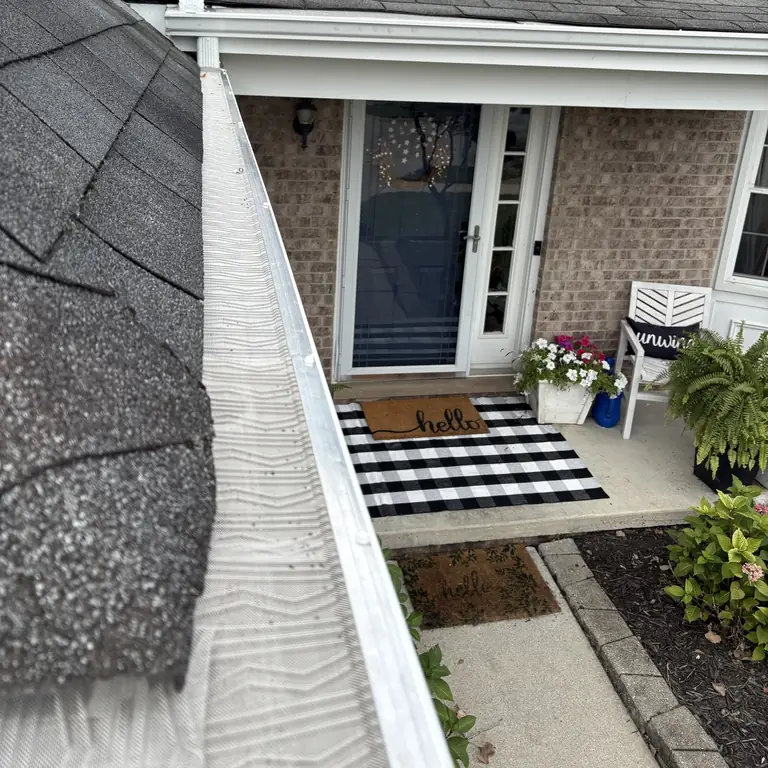 Seamless white gutter with a micro-mesh gutter guard over a brick front porch