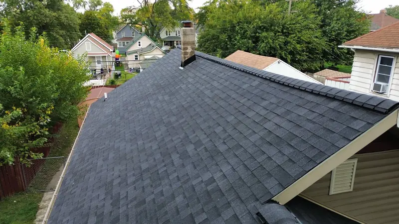 Finished dark grey architectural shingle roof with ridge cap shingles and a chimney, seen from above
