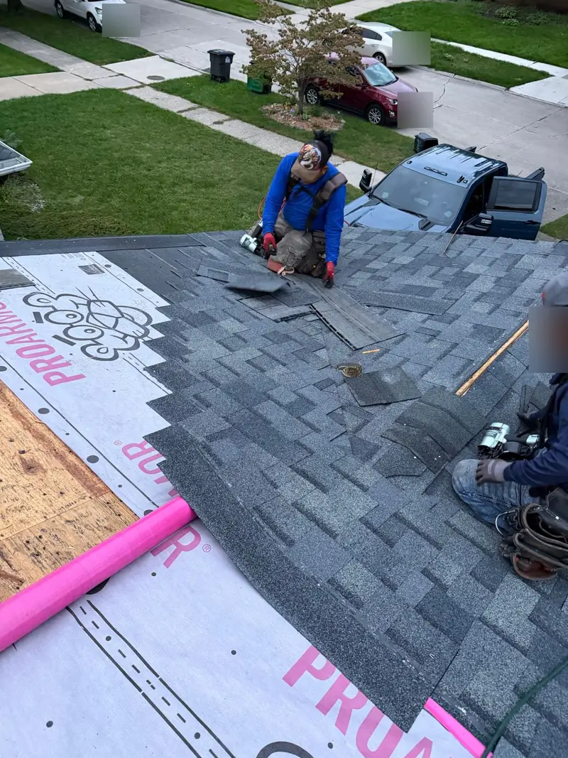 Roofers installing grey architectural shingles over synthetic underlayment, with bare roof decking still visible at one edge
