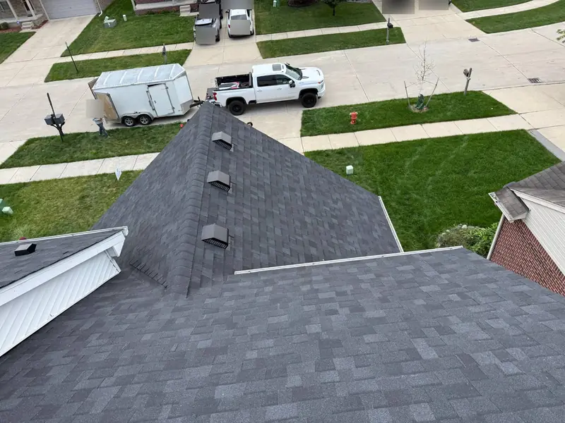 Finished dark architectural shingle roof seen from the upper ridge, with three box vents near the ridge and a work truck and trailer at the curb